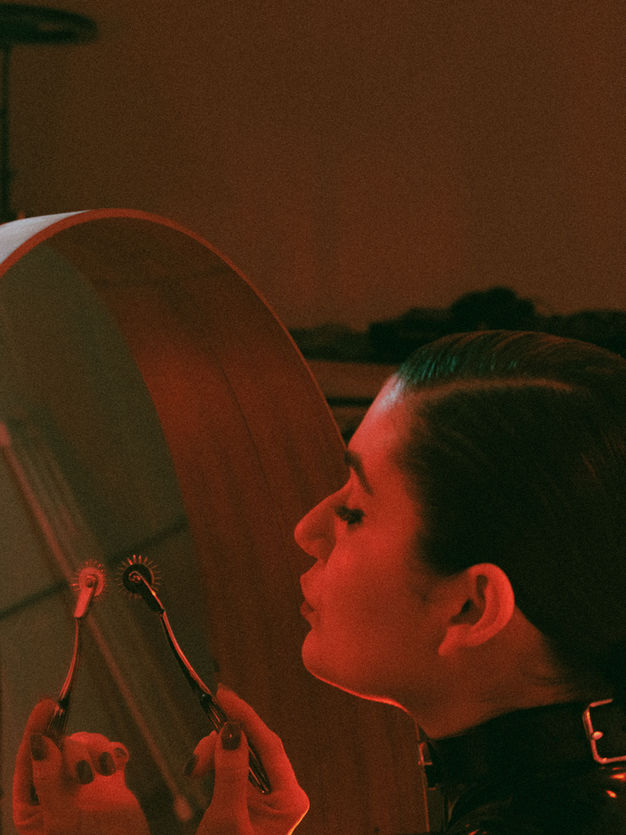 Profile shot of Boston & NYC Professional Dominatrix Mistrix Violeta Félix looking into a mirror with a Wartenberg wheel on her hand.