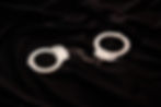 Silver handcuffs linked by a short chain on black fabric, creating a stark, restrained mood.