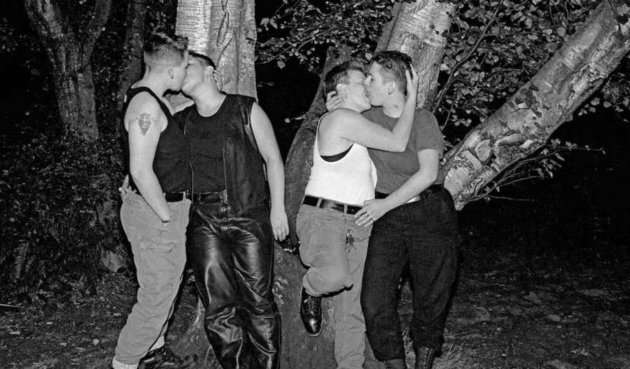 Black-and-white photo of two couples kissing and embracing among trees at night.