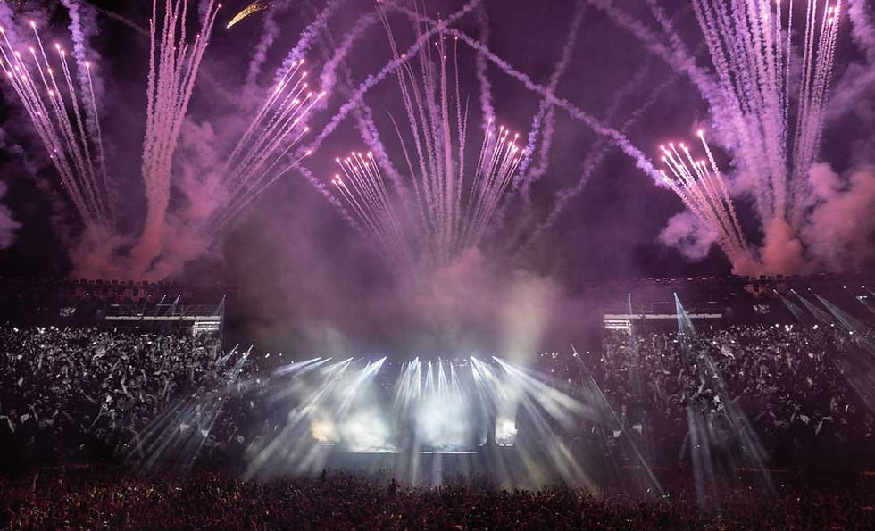 Concert with crowd, stage lights, and fireworks in the sky. Purple smoke fills the air, creating an energetic and lively atmosphere.
