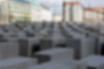 Rows of gray concrete slabs at the Holocaust Memorial, with apartment buildings and a cloudy sky behind them.