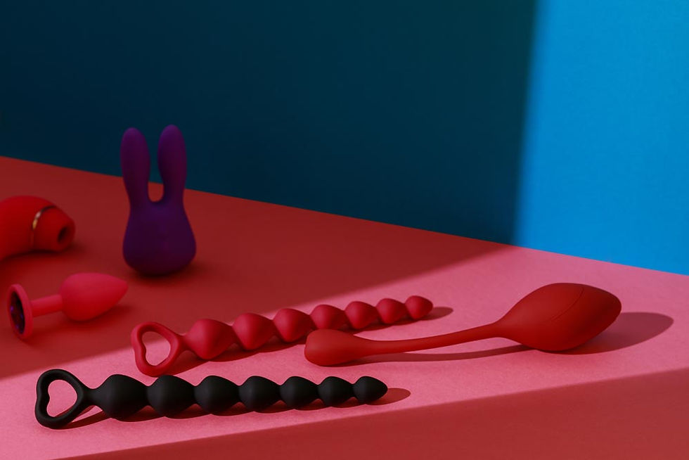 Colorful sex toys on a pink surface under blue light, including plugs and beaded devices arranged in a still life.