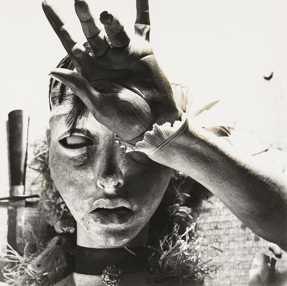 Black-and-white close-up of a masked person covering their face with a raised hand, creating a dramatic, eerie mood.