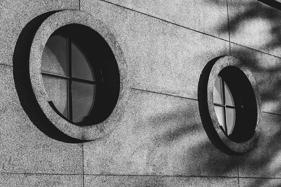 Round windows on a textured concrete wall with diagonal shadows. Black and white image creates a modern, abstract feel.