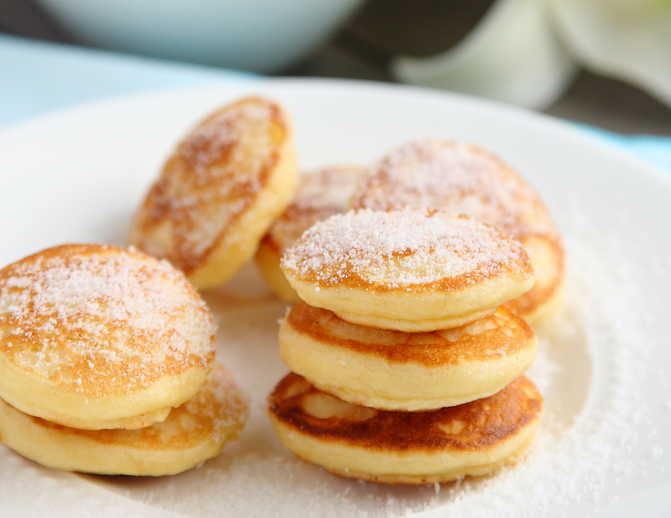 Small, fluffy pancakes dusted with powdered sugar on a white plate served at a catering event.