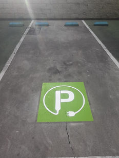 Professional line marking for an electric vehicle (EV) charging bay, featuring a high-visibility green "P" stencil with a plug icon on a concrete parking surface.