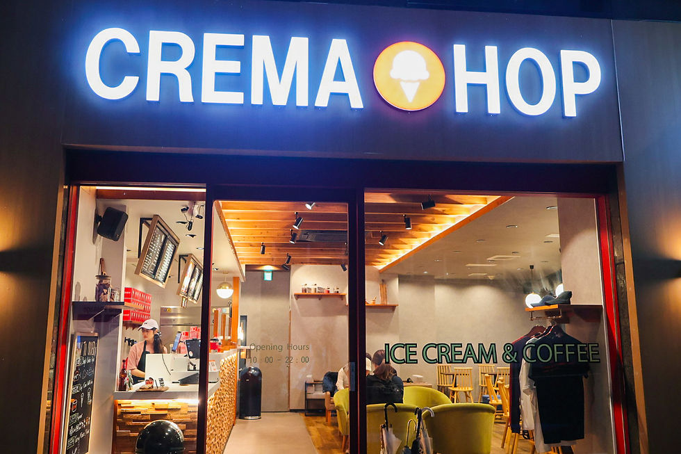 Bright CREMA HOP ice cream and coffee shop at night, with staff inside, seated customers, and warm wood interior.