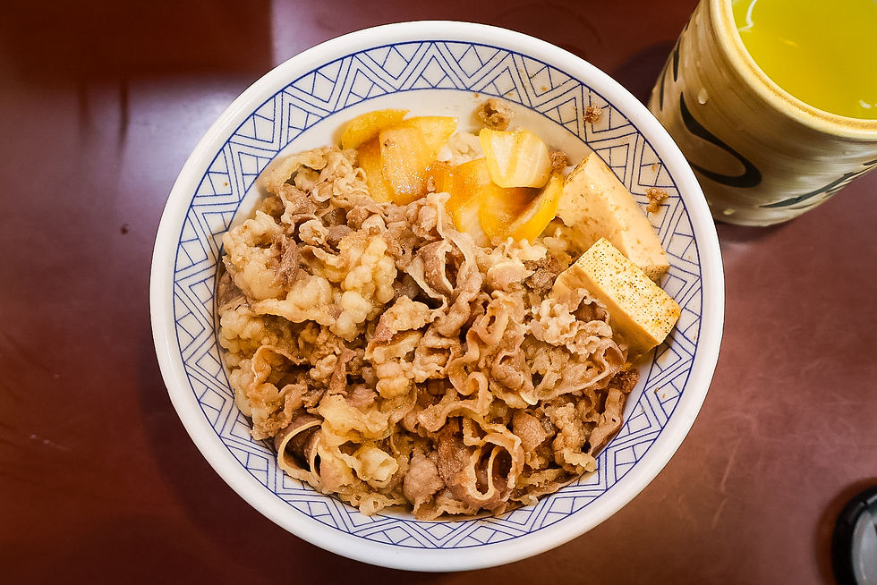 Bowl of beef and tofu over rice on a patterned plate, with a yellow drink cup beside it on a dark table.