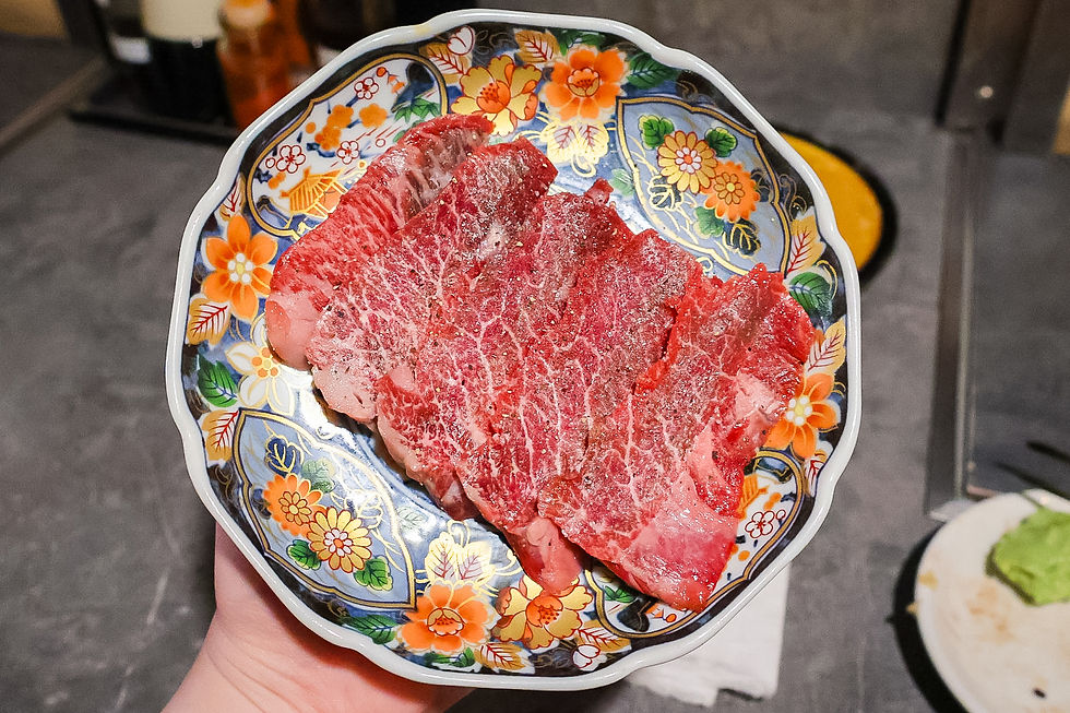 Hand holding a floral bowl of raw marbled beef slices on a restaurant table, with a calm dining mood.