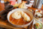 Japanese noodle dish in a ceramic bowl with tempura, dipping sauces, and side dishes on a wooden table.
