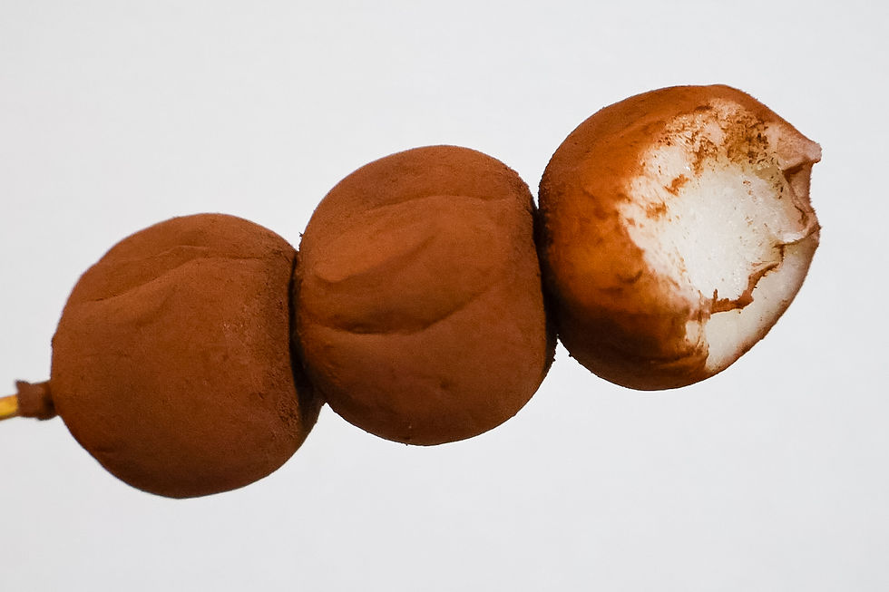 Skewered chocolate-covered dango against a white background, with one dango partially bitten, revealing a fluffy interior.