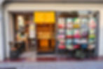 Japanese dessert shop storefront with yellow noren, colorful pastry posters, and small outdoor tables and stools