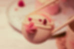Chopsticks hold a pink and white macaron with cream and raspberry bits. Background shows a blurred plate, creating a delicate mood.