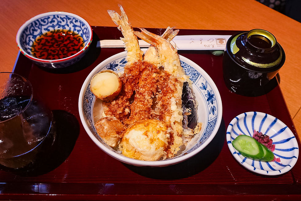 Japanese tempura rice bowl with shrimp, vegetables, soup, tea, and pickles on a red tray in a warm restaurant setting