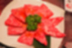 Marbled beef sashimi arranged like a flower on a white plate, topped with parsley, on a restaurant table.