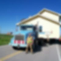 A man poses in front of a stationary trailer loaded with a house