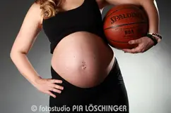 Babybauch im Vergleich mit dem Basketball mit markanter Lichtsetzung.