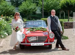 Brautpaar mit einem roten Cabriolet.