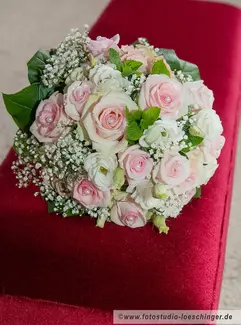Brautstrauß in weiß-rosa liegt auf rotem Samt.