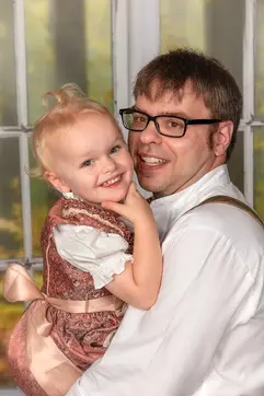 Kleines Mädchen im Dirndl lacht auf Papas Arm in die Kamera.