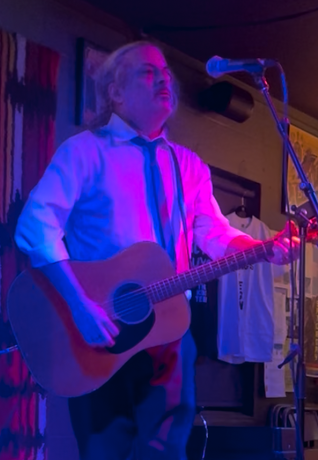 Photo of an incredibly handsome man with an acoustic guitar at a microphone in a nightclub
