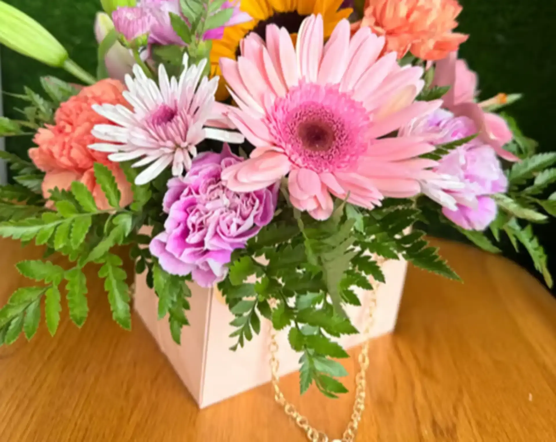 Pink gerbera daisies, purple carnations, peach mini-carnations, and greenery in a handbag-style box