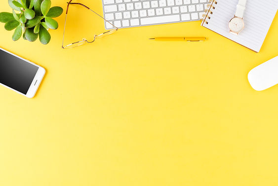 Yellow desktop with keyboard, phone, glasses, pen and notebook