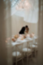 A married couple kissing by their wedding breakfast tables, the candles are lit and the orangery has been draped with off white linen