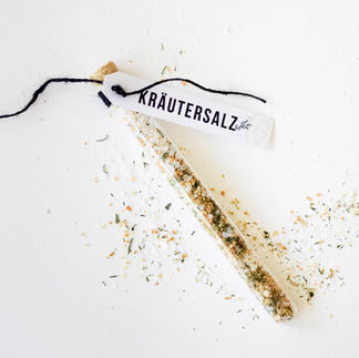 Zitronen Kräutersalz in einem eleganten Reagenzglas auf weissem Hintergrund. Mit einer weissen Etikette wo drauf steht: Kräutersalz