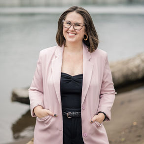 Headshot of wedding planner Andy in all black with a pink blazer in front of the Willamette River in PDX