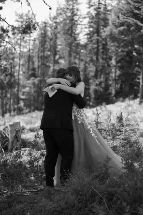 B&W photo of a bride and groom hugging in the woods 