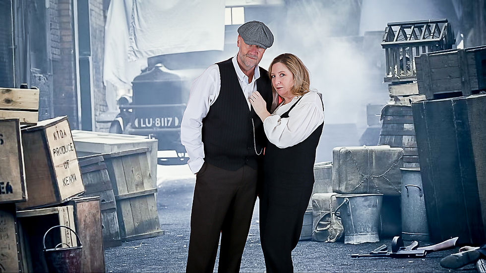 A man and woman in vintage attire stand in an alley with crates and a car. The mood is nostalgic. Text on a crate reads "KIDA PRODUCE OF KENYA."
