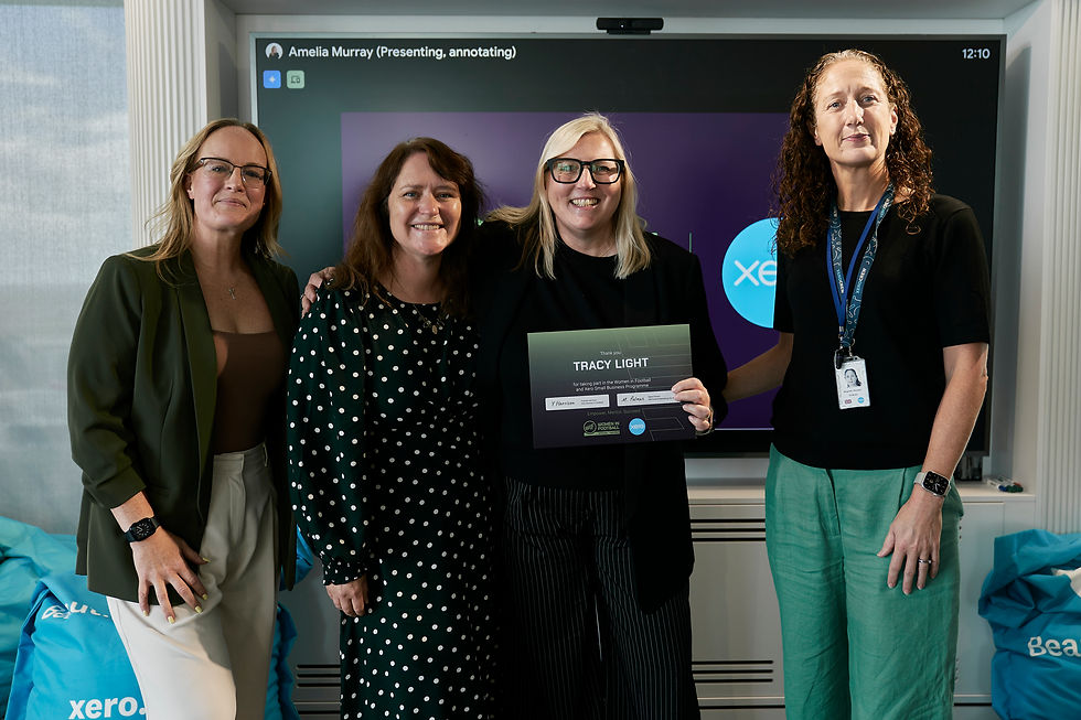 Four women smiling indoors, one holding a certificate. Background shows a screen with "Xero" logo. Blue bags are visible, creating a celebratory mood.