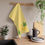 Thumbnail: A kitchen scene featuring a yellow towel with a lemon and leaf design hanging on a wooden rack, surrounded by kitchen items.