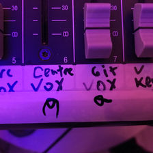 The channels of a mixing desk marked with a rough drawing of a person with dreadlocks and a person in a baseball cap