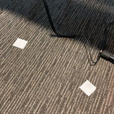 Two pieces of white sticky tape on grey, commercial carpet, and a bit of headphone cable