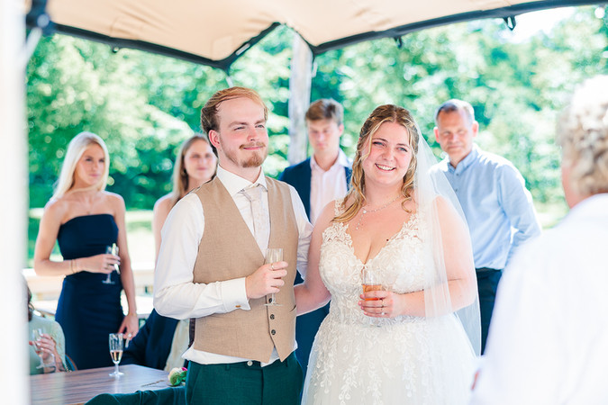 Bruidspaar luistert naar de speech met een glas champagne in hun hand