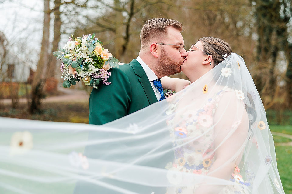 bruidspaar kust en wordt omringt door een waaiende sluier vol kleurrijke bloemen