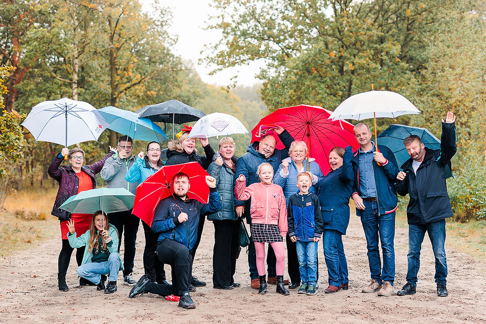 Fotoshoot in de regen met de familie, iedereen onder een grappige en kleurrijke paraplu's.