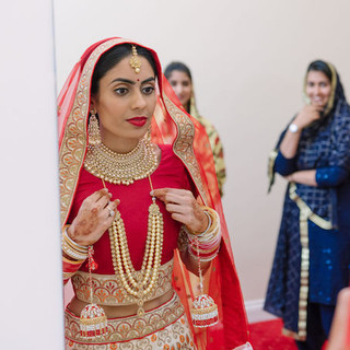 Tradtional Indian bridal garb, bold makeup and sleek hair under a long traditional veil