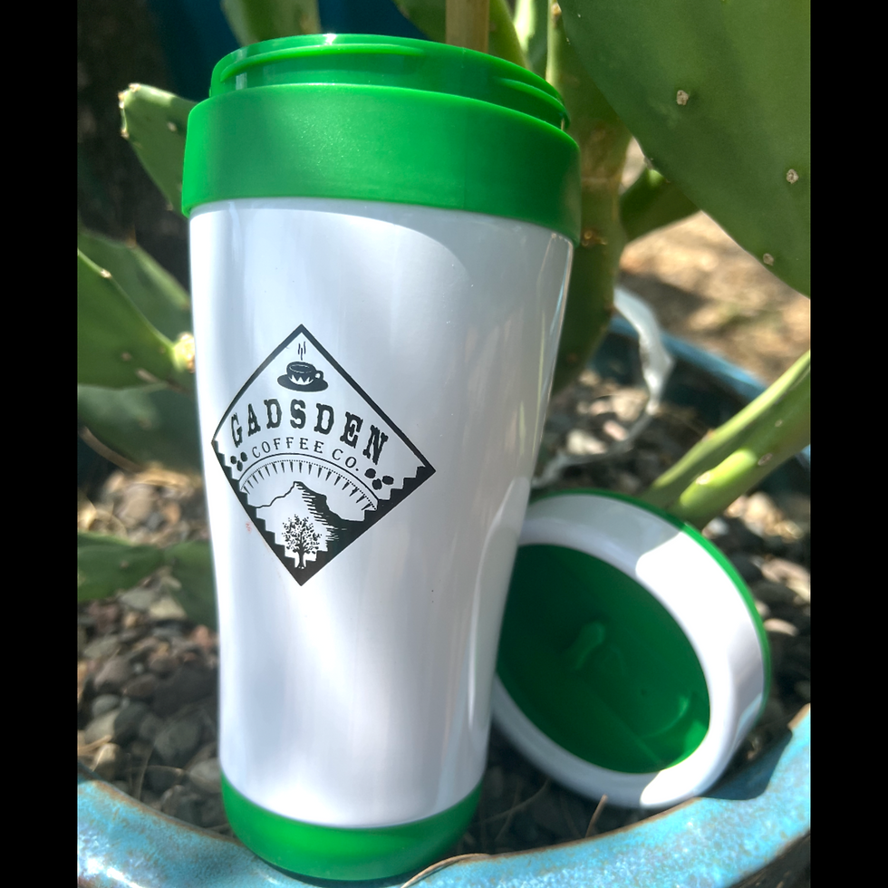 A green and white travel cup sits next to its lid, inside of a cactus planter. 