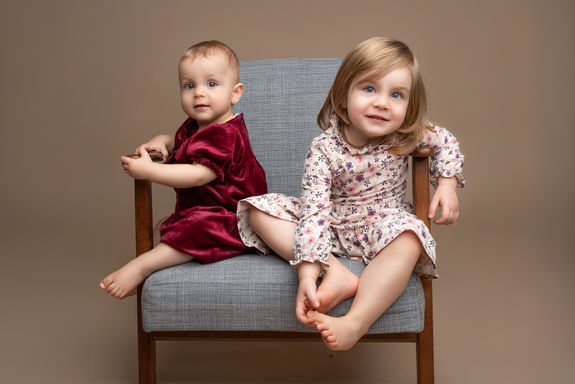Fotostudio Kinderfotografie. Schwestern sitzen auf ein RetroSessel mit Braune Hintergrund