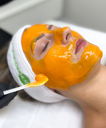 Applying a pumpkin face mask with a spatula to a woman's face.