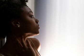 Black woman with natural hair staring off into the distance against a white wall.