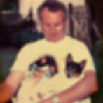A toy fox terrier lounging in the lap of a man, sitting in a chair outside.