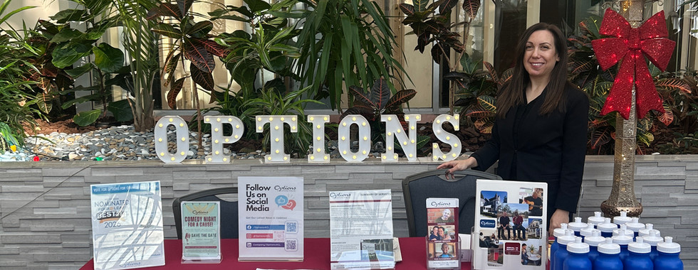 A woman standing behind a table with a red table cloth that reads "Options for Community Living." Next to her are letter lights that read "Options."