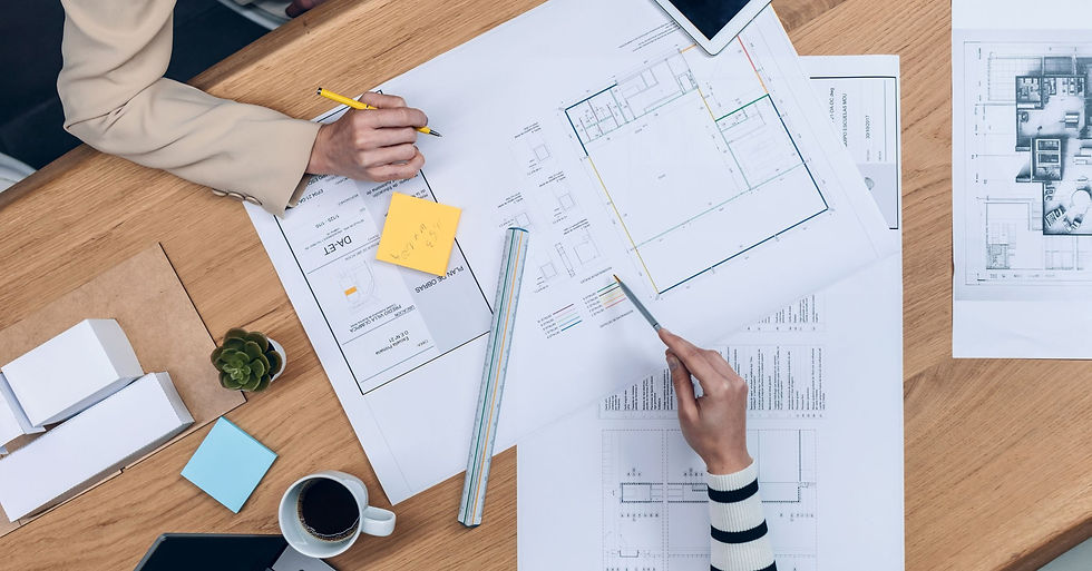 Overhead view of two professionals reviewing architectural plans and floor layouts with a ruler, tablet, and design documents during the custom home planning and design process.