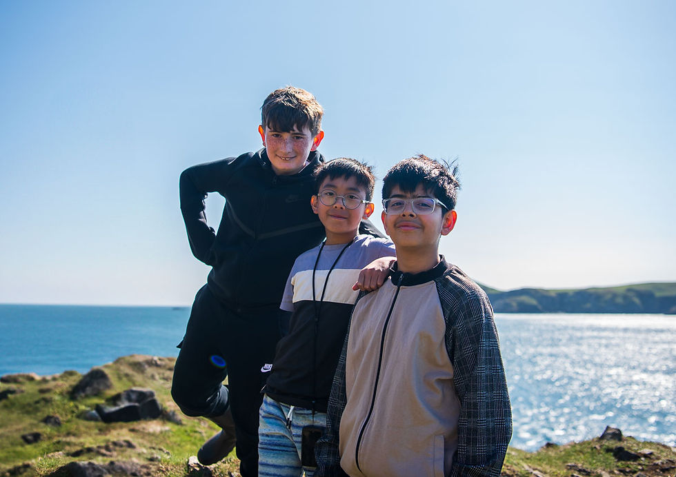Three boys posing for a photo, on top of a cliff in Wales on their farm retreat; the boys are looking directly at the camera and smiling
