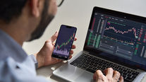 Person analyzing crypto charts on a smartphone and laptop. Screens display colorful graphs and data 