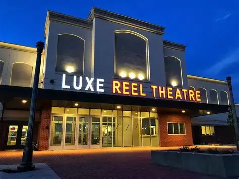 Luxe Reel Theatre at dusk, illuminated by bright marquee lights against a deep blue sky. Brick facade and glass entrance visible.